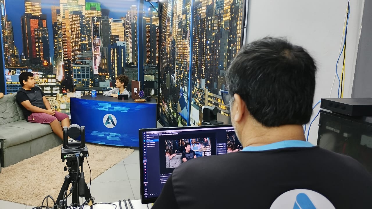 Jovens acompanham operação de câmera e OBS durante visita ao estúdio da TV Attual.